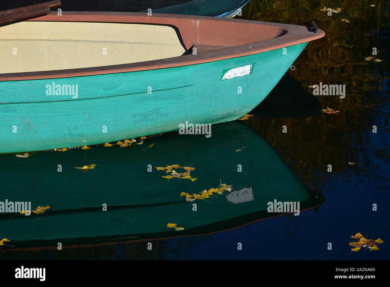 La parte anteriore di un verde in barca nelle acque di un lago che riflette nell'acqua. Alcune foglie di giallo sono galleggianti sulla superficie dell'acqua. Foto Stock