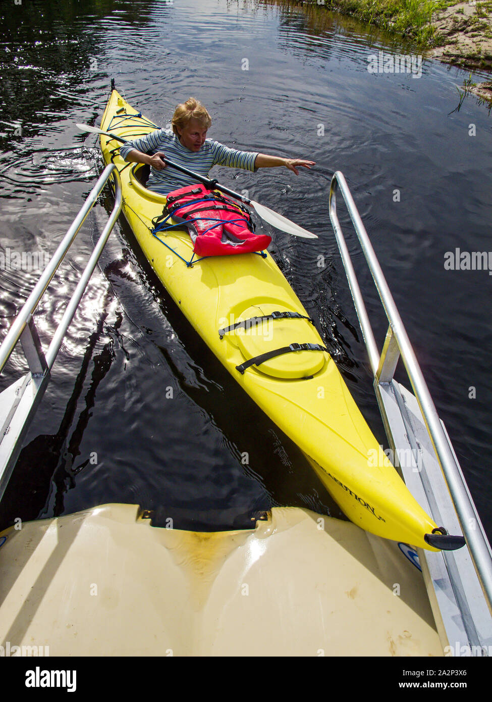Donna docking kayak; raggiungendo per la ringhiera; fai-da-te dock; fiume; ricreazione; sport, esercizio natante; giallo barca, Northport, FL, Florida, v Foto Stock