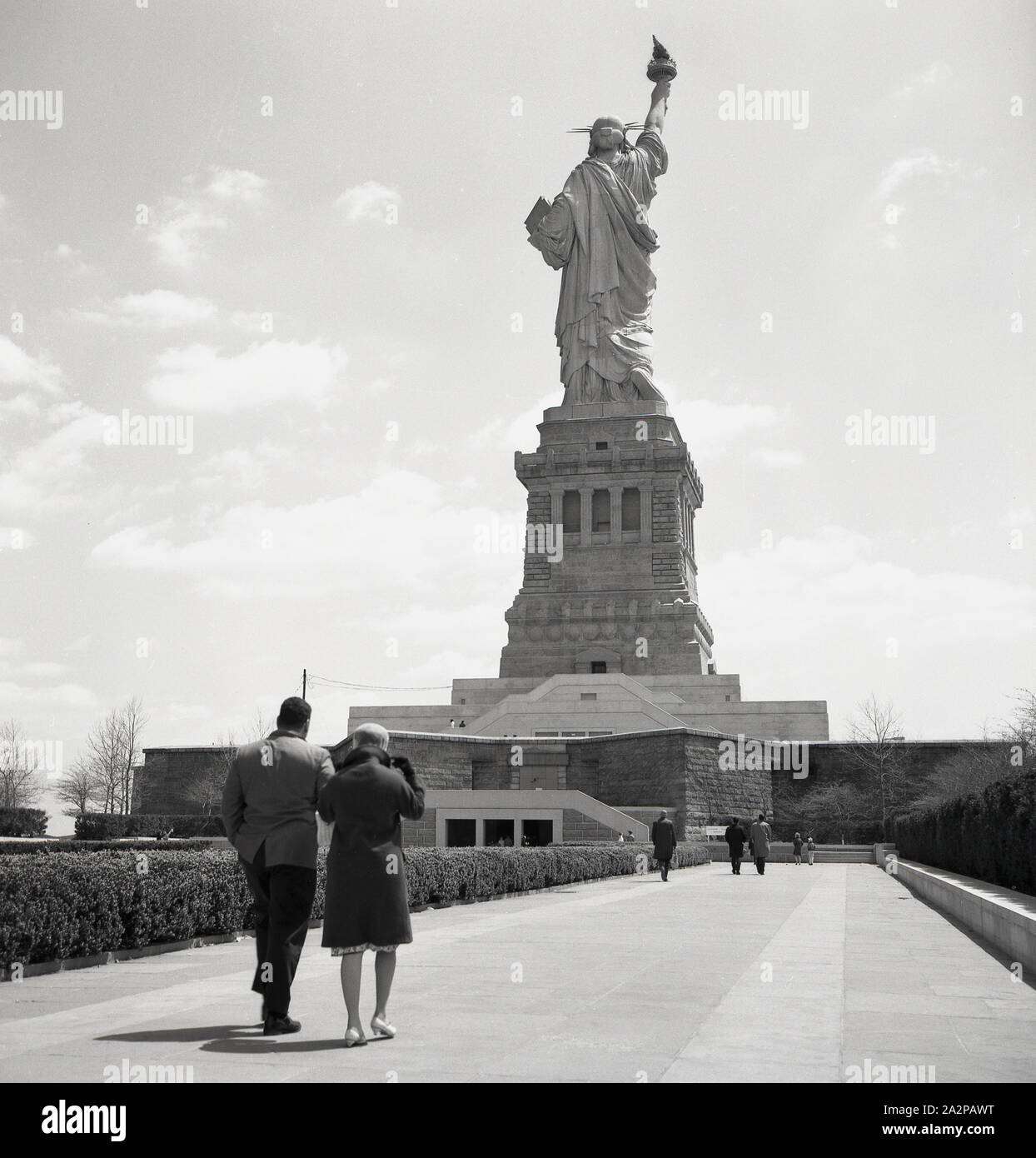 Anni '1960, storica, una coppia che cammina lungo un sentiero verso la Statua della libertà, una grande scultura neoclassica su Liberty Island nel porto di New York City, Stati Uniti. La statua di rame era un dono del popolo francese. Progettata dallo scultore francese Frédéric Auguste Bartholdi, la sua struttura metallica fu costruita da Gustave Eiffel, lui della famosa torre di Parigi. Foto Stock