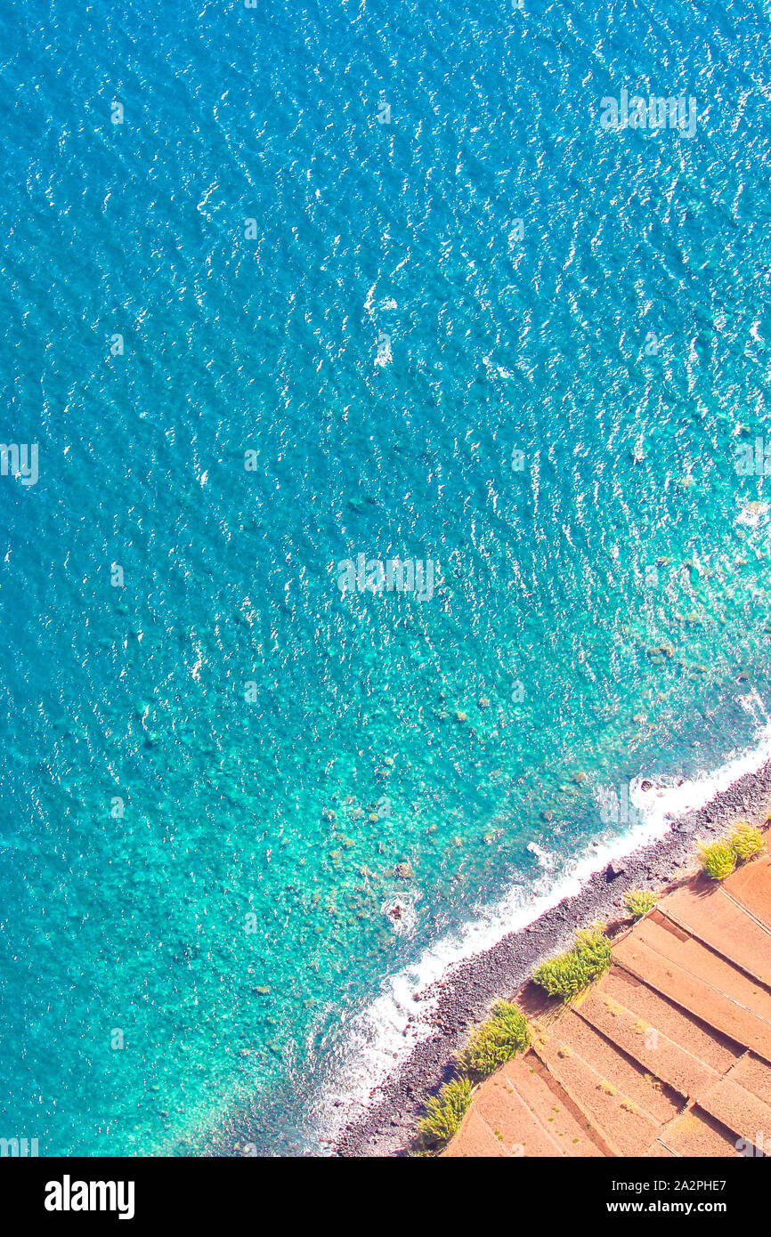 La fotografia aerea del turchese oceano Atlantico costa in Madeira, Portogallo. Spiaggia di pietra e campi adiacenti sulla costa meridionale dell'isola portoghese. Vista aerea, seascape. Foto Stock