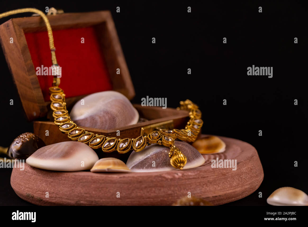 Bella tradizionali collana dorata con scatola in legno e conchiglia sulla sabbia di pietra con sfondo scuro. Tradizionale concetto di regalo Foto Stock
