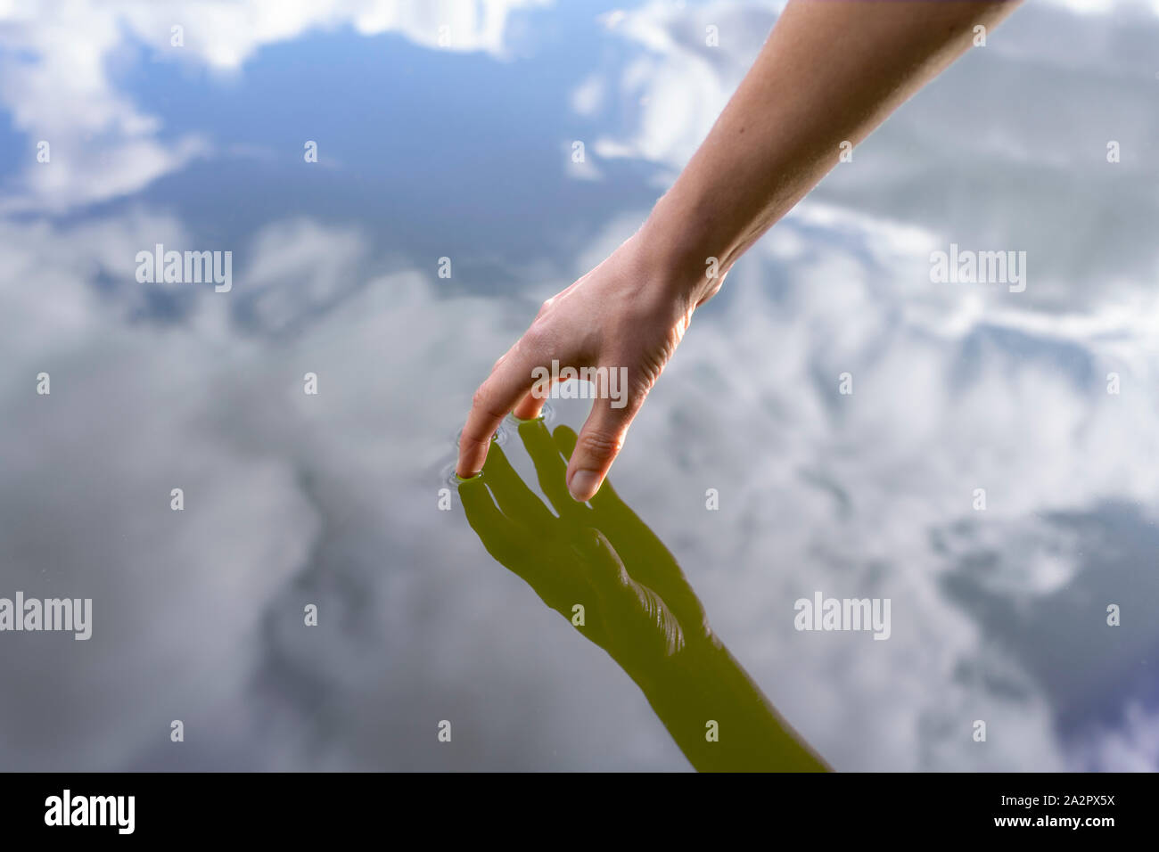 Womans aveva toccando la superficie di un lago, riflessioni di mano e cielo Foto Stock