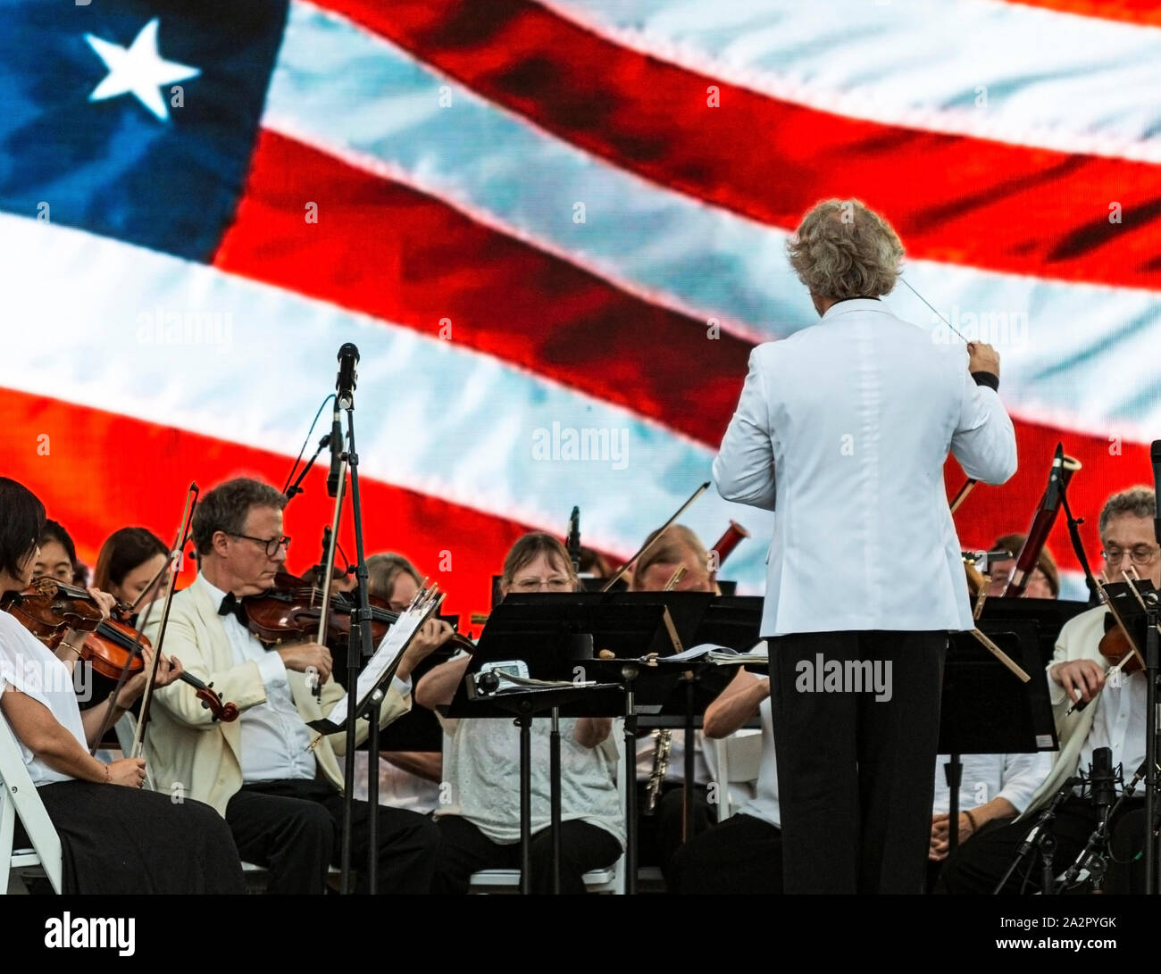 East Islip, NY, Stati Uniti d'America - 13 Luglio 2019: Il Long Island Concert Orchestra esegue gratuitamente su Heckscher parco dello stato con una bandiera americana sullo sfondo. Foto Stock