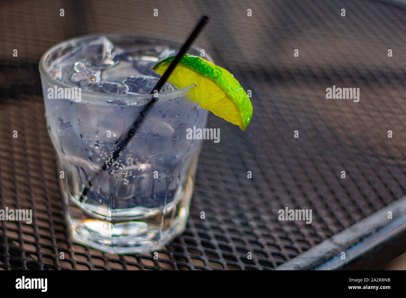 Un bicchiere di gin tonic, guarnita con calce, si siede su un tavolo di metallo su un patio esterno. Foto Stock