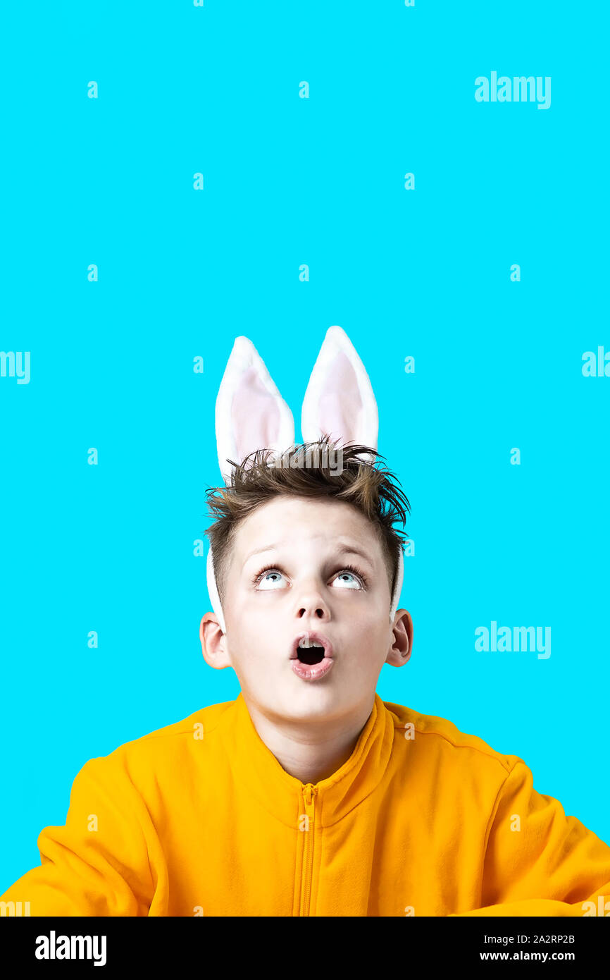 Ragazzo sorpreso in una giacca gialla e le orecchie di lepre su uno sfondo blu Foto Stock