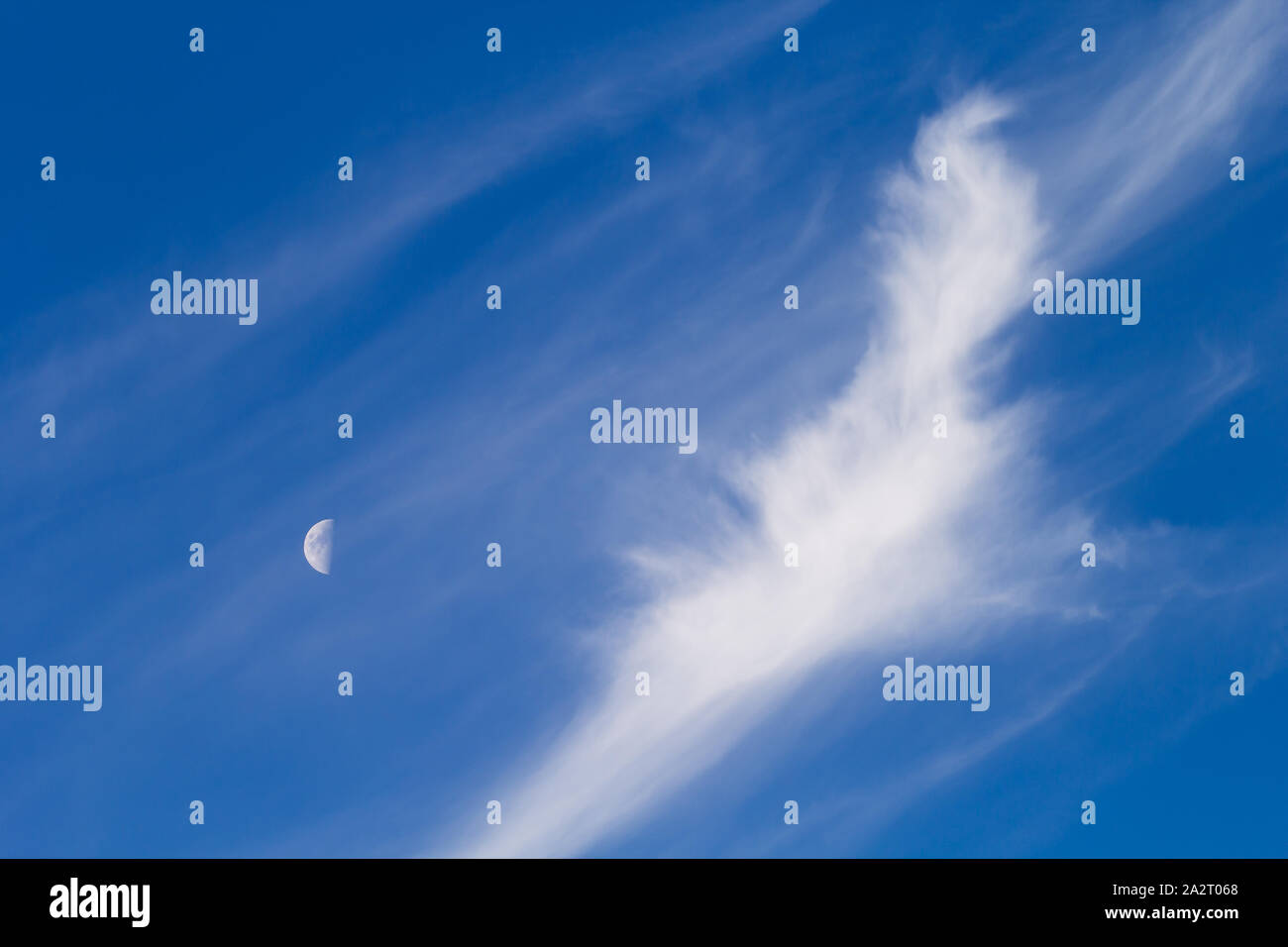 Primo quarto di luna durante il giorno con il cielo blu e nuvole Cirrus. Foto Stock