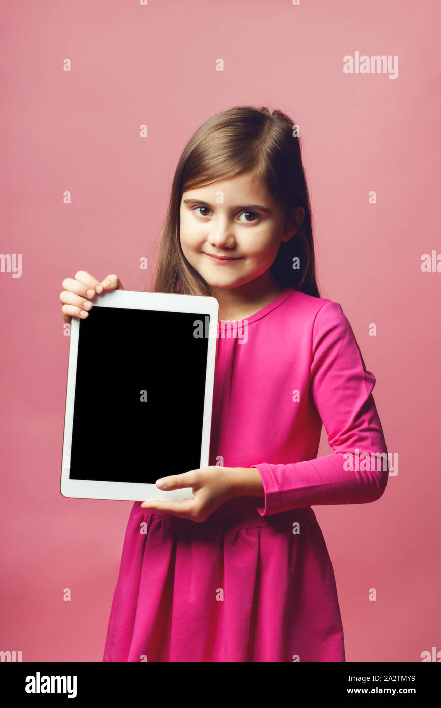 Graziosa bambina tenendo un tablet con uno schermo nero. Abito rosa e sfondo rosa. Posto per il testo. Il concetto di offerte speciali per le ragazze, vendite promozionali, ecc. Foto Stock