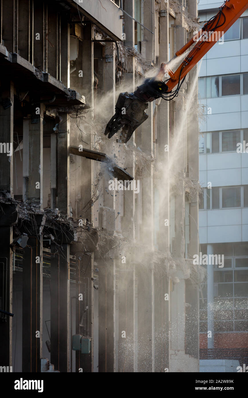 Edificio in fase di demolizione in Birmingham con high reach escavatore, UK, con uno spruzzo di acqua controllo della polvere Foto Stock