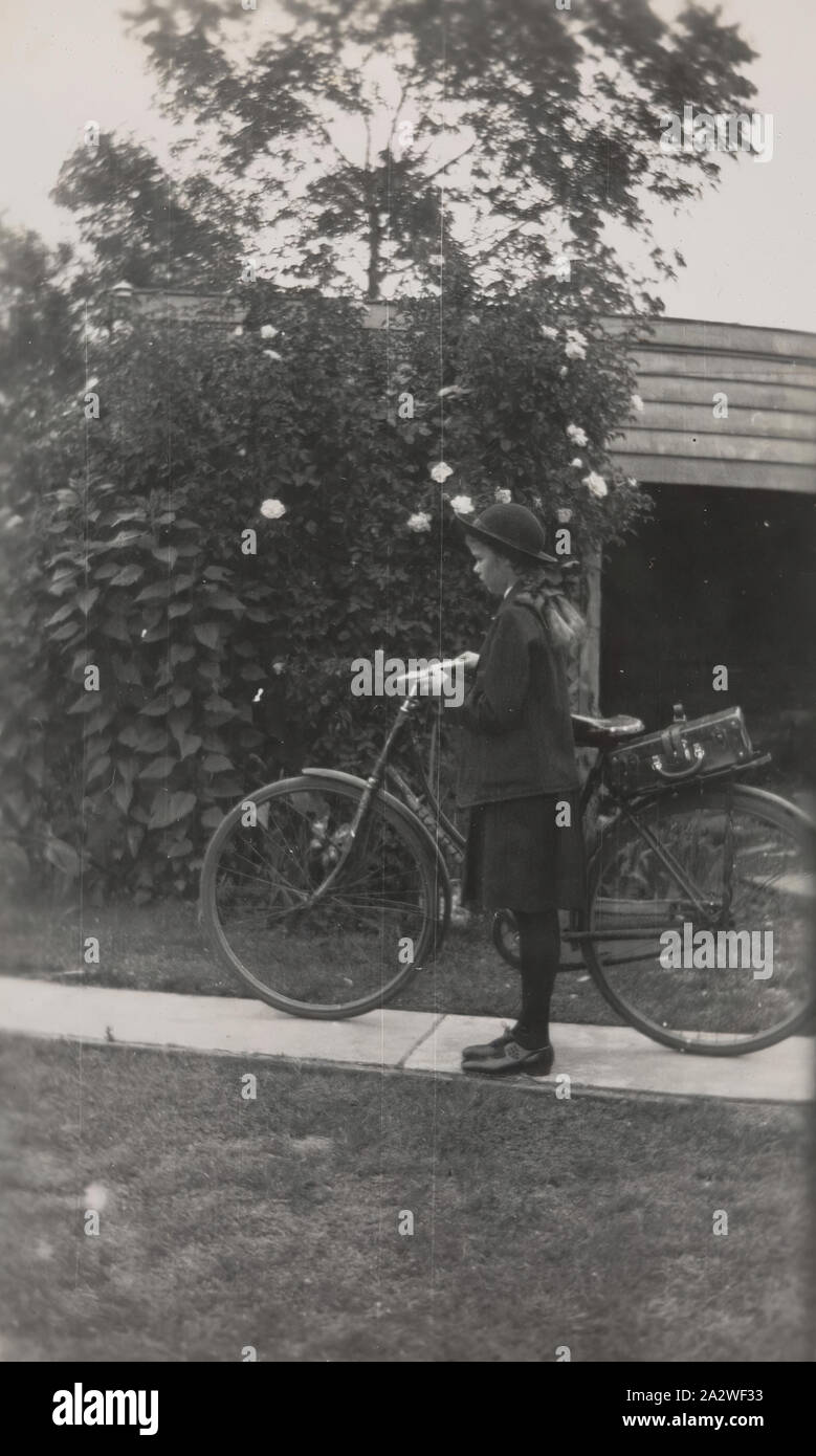 Fotografia digitale - ragazza in uniforme scolastica e Hat, in piedi con la bicicletta nei pressi di un capannone, nel cortile Colac, 1940, ragazza in uniforme scolastica e Hat, in piedi con la bicicletta, nel cortile. Questa fotografia mostra Alison Doig nel 1940, con la stessa moto come in immagine MM111002, un Hartley 'free-wheeler'. La bicicletta è stata una mano-me-giù dalla sua sorella Jean. Alison era vestito con il Colac High School uniforme con un cappello, blazer, maglietta, tunica in blu navy. La sua scuola borsa era sul retro della moto, legato su di un bagaglio Foto Stock