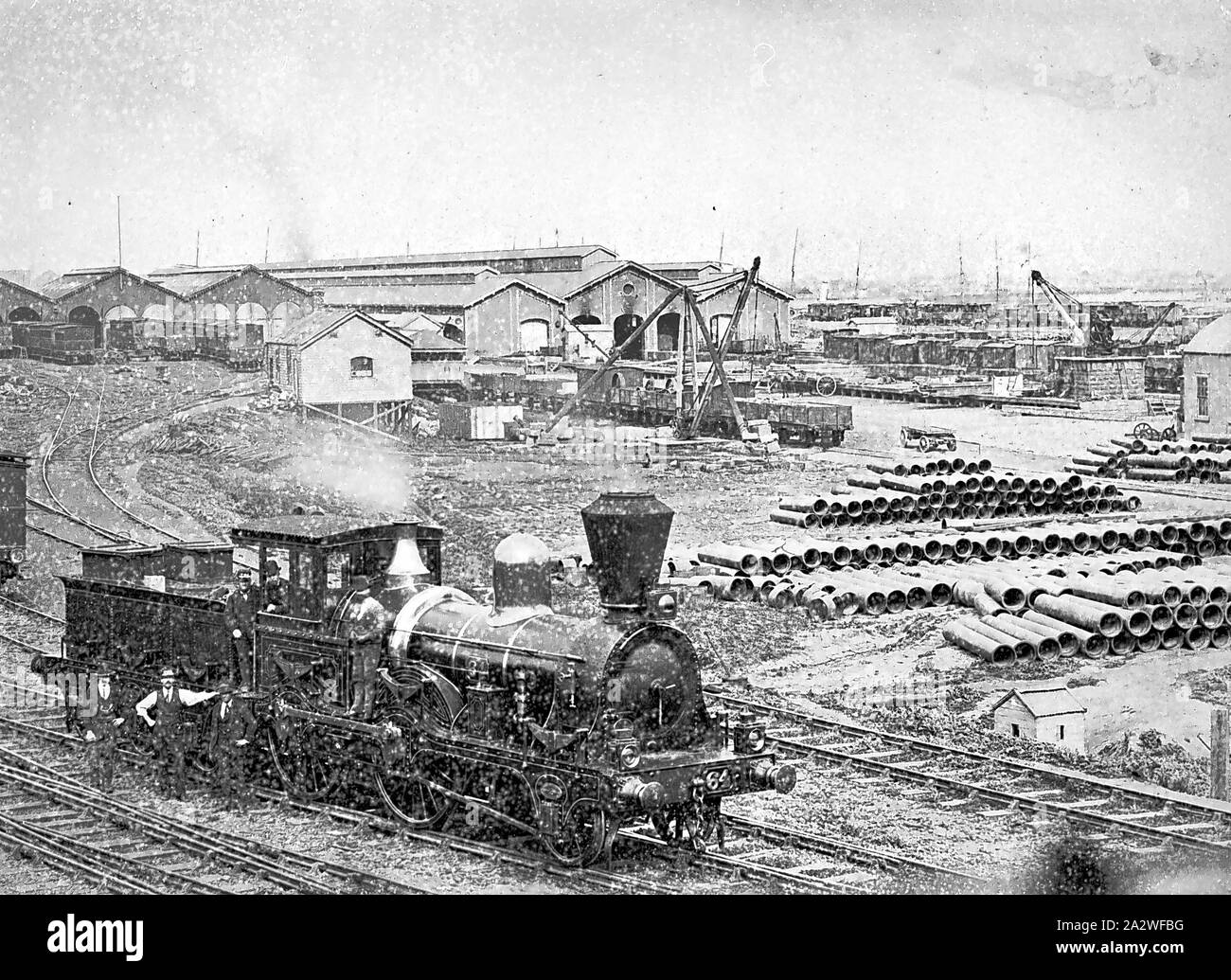 Negativo - Melbourne, Victoria, circa 1885, Motore No.64 nei cantieri ferroviari, il Victorian merci sparso in background. Vi è una pila di canalizzazioni fognanti sulla destra Foto Stock