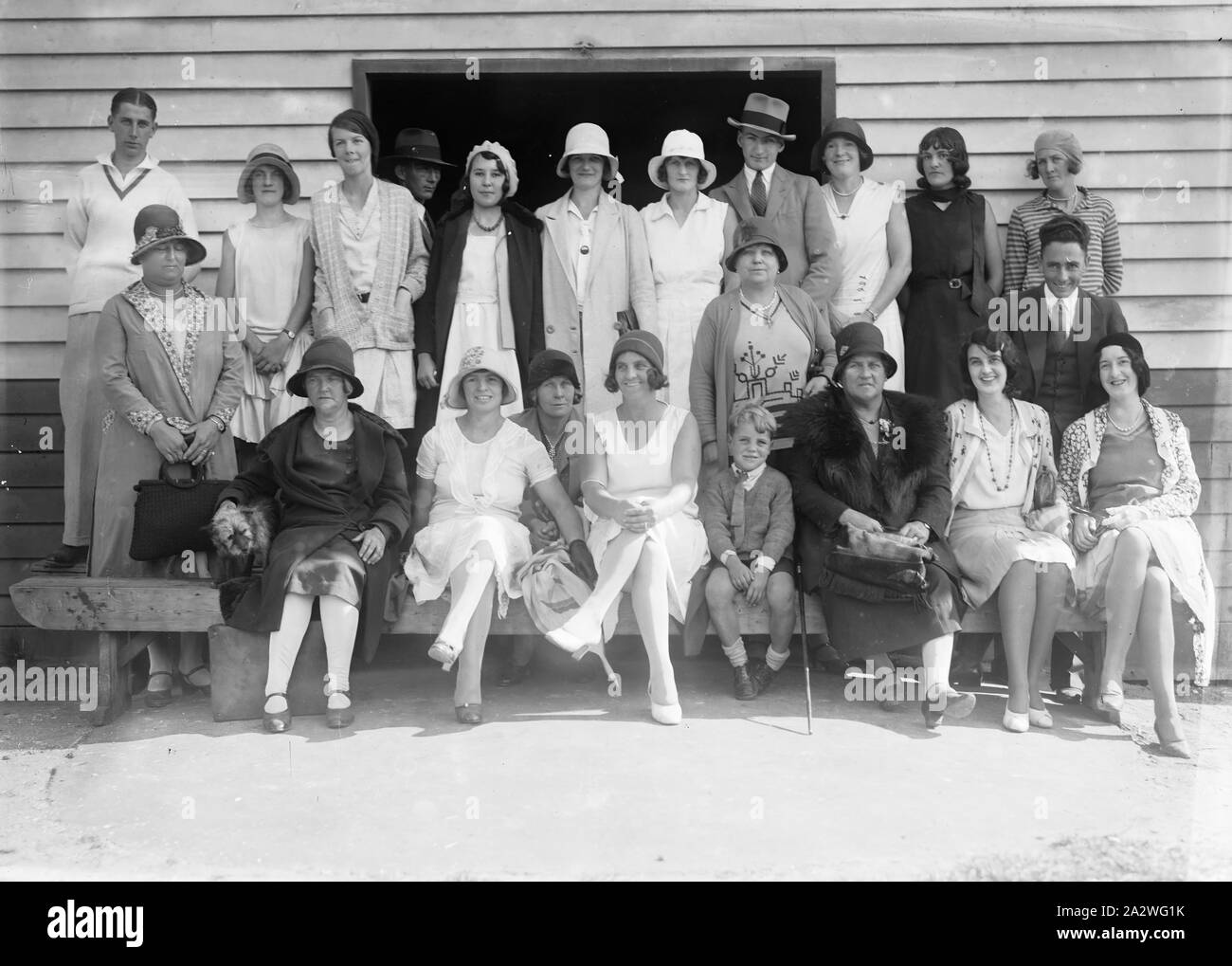 Negativo di vetro - Ritratto di gruppo in campo sportivo, circa 1930, una in bianco e nero, metà piastra negativa con un ritratto di gruppo di uomini, donne e bambini su un campo sportivo di fronte a un capannone di sport. Questi sono probabilmente i familiari e gli amici dei bambini che partecipano al visto gare su disegni di negativi Foto Stock