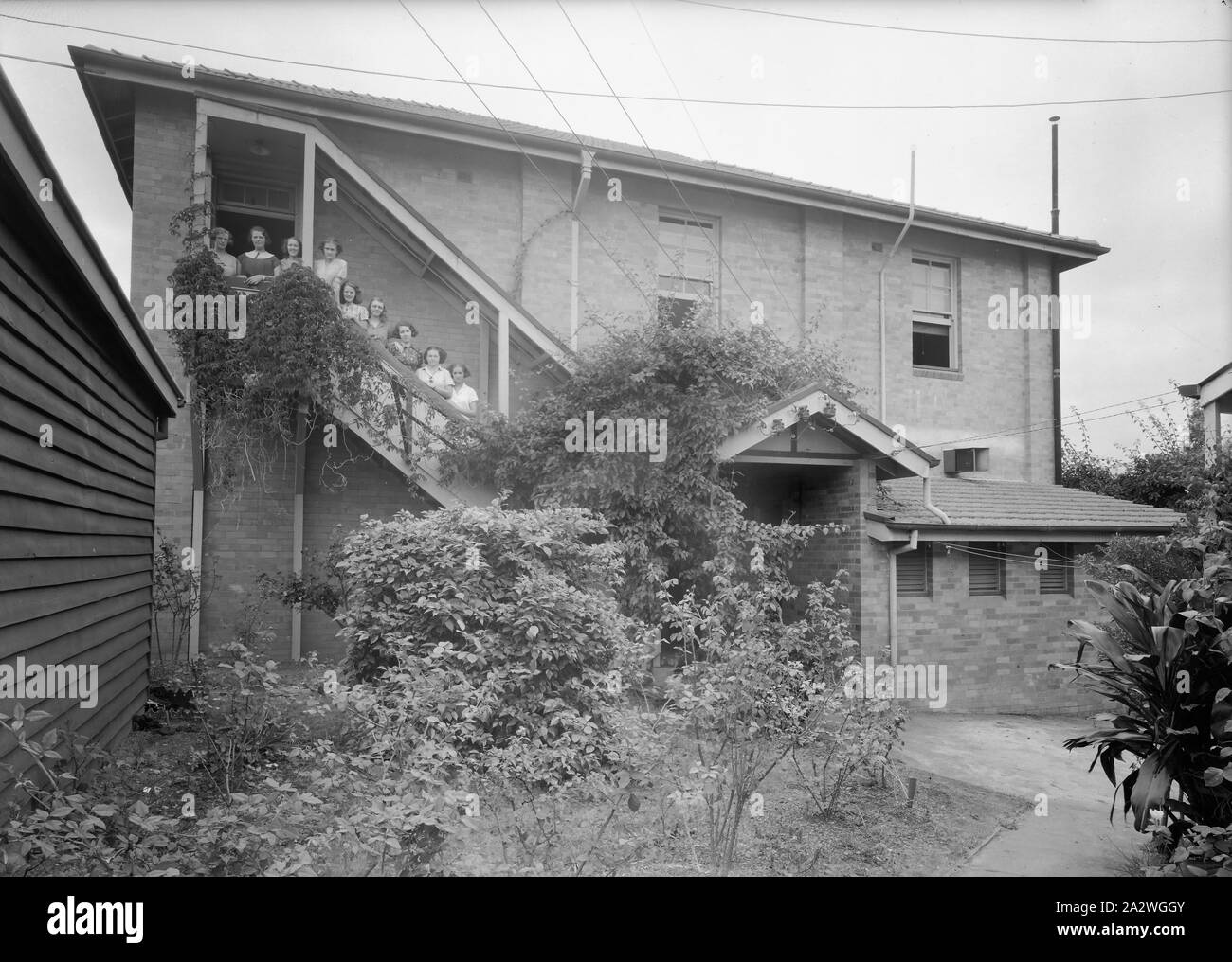 Negativa, sviluppo e stampa Team, Townsville, QLD, 1930s, film in bianco e nero in negativo la Kodak Australasia Pty Ltd sviluppo e stampa team dal laboratorio di elaborazione a Townsville, Queensland, negli anni trenta del novecento. Il gruppo di 9 donne sono in piedi sulle scale sul retro di un edificio di due piani in mattoni con cespugli di rose e vigneti nel giardino in basso in primo piano. raccolta di materiali promozionali Foto Stock