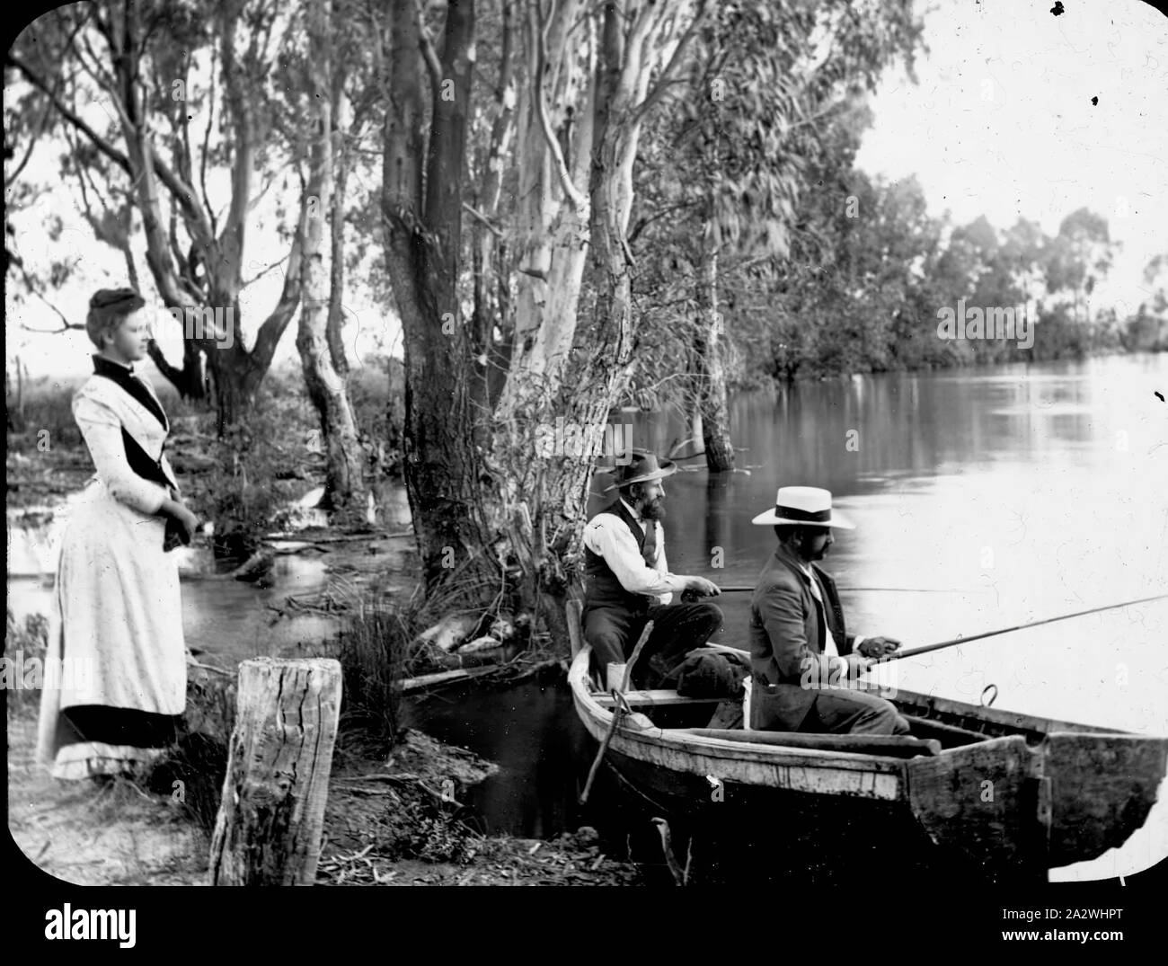 Lantern Slide - Pesca nel fiume, Victoria, Australia, circa 1890, immagine in bianco e nero di A.J. Campbell seduto in una barca, senza una camicia su, mentre lui e un amico erano la pesca, possibilmente nel Fiume Yarra, con una donna in piedi sulla banca cerca su. Questo è uno dei molti lanterna in vetro le diapositive che formano la A.J. Campbell Collezione detenute da musei Victoria Foto Stock