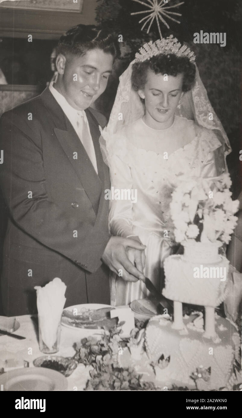 Fotografia digitale - Ritratto di nozze, Maria Crocker McKenzie & marito, taglio torta nuziale, Belgrave, 1953, fotografia in bianco e nero di Maria Crocker McKenzie e di suo padre e il loro taglio torta nuziale in Belgrave nel 1953. Nell'immagine di Maria indossa il matrimonio di famiglia velo che è stata fatta passare verso il basso attraverso una linea femminile e indossato da oltre 100 donne oltre cinque generazioni. Il merletto Limerick velo nuziale è stata importata dall'Irlanda per le nozze del migrante scozzese Janet Scrimgeour quando ha sposato danese Foto Stock