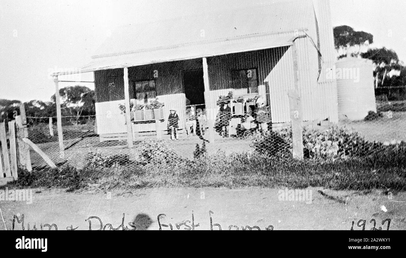 Negativo - Chinkapook, Victoria, 1927, una famiglia sulla veranda della loro ferro corrugato home. Essi hanno gli inizi di un giardino frontale, comprese le piante in vaso lungo la veranda. Il cortile anteriore è recintata con rete metallica e vi è un serbatoio di acqua sul retro della casa Foto Stock
