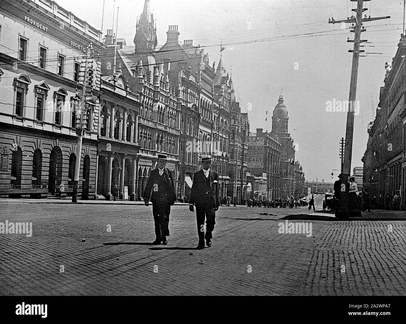 Negativo - Melbourne, Victoria, circa 1900, Collins Street, guardando ad ovest. Due uomini, sia indossando diportisti di paglia, sono attraversando la strada in primo piano. La torre della Federal Hotel è visibile in background Foto Stock