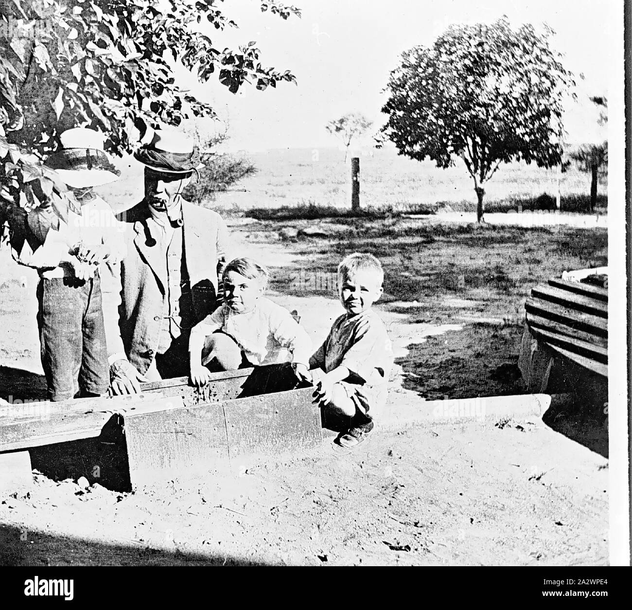Negativo - Isisford District, Queensland, circa 1915, un uomo e tre ragazzi a fianco di una trappola di rana installato tra il serbatoio di acqua e la casa sulla "Portland Downs' station Foto Stock