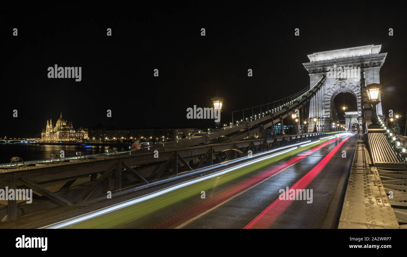 Illuminato il Ponte delle Catene Szechenyi di notte a Budapest con il Parlamento in background e Liscia rossa luci di traccia, Ungheria Foto Stock