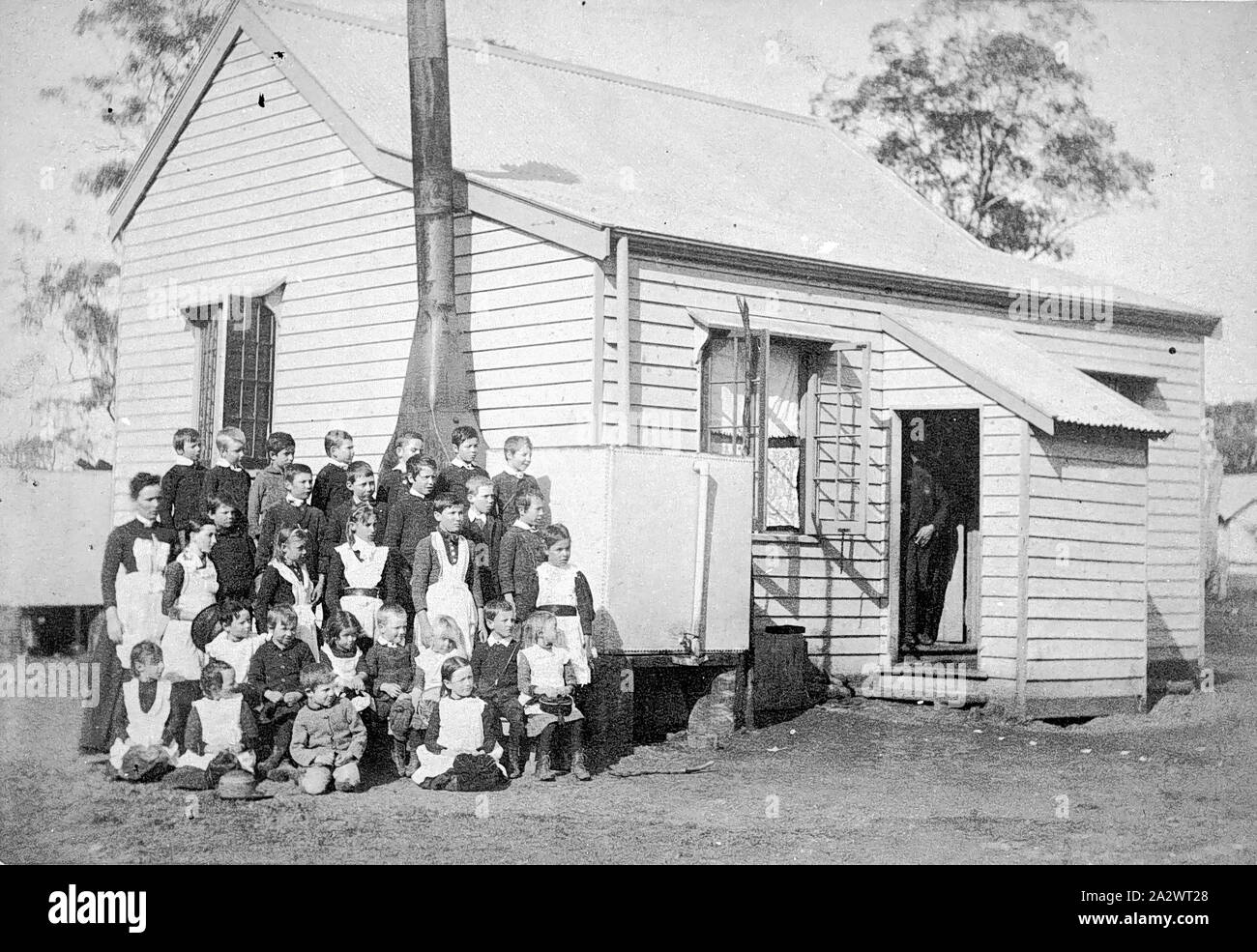 Negativo - Studenti e insegnanti al di fuori Wychitella scuola statale, Wychitella, Victoria, pre 1910, gruppo di 29 bambini della scuola di fronte al Wychitella scuola statale. Un uomo che può essere un insegnante si trova dentro la porta della scuola. Una donna che può anche essere un insegnante, è in piedi sul lato sinistro del gruppo. È possibile che la donna è Elizabeth Jane Mann che era un insegnante presso la scuola durante il 1880 Foto Stock