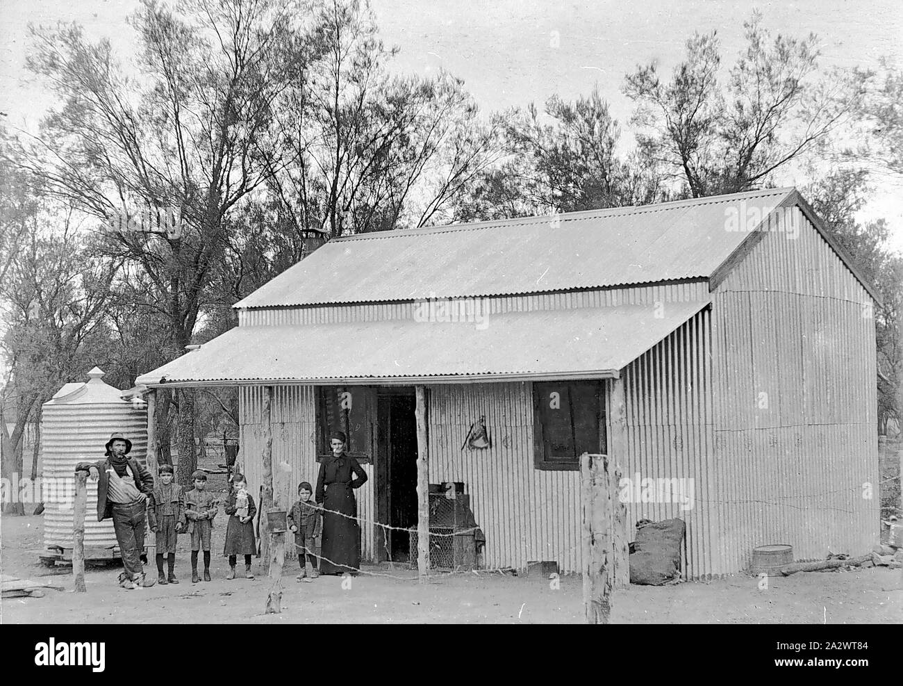 Negativo - Merbein District, Victoria, circa 1910, Bill Smith e la sua famiglia al di fuori di Bob Telford capanno. Il rifugio è costruito interamente di ferro corrugato, con veranda in legno supporti. Si tratta di un ambiente rurale con un serbatoio di acqua a lato Foto Stock