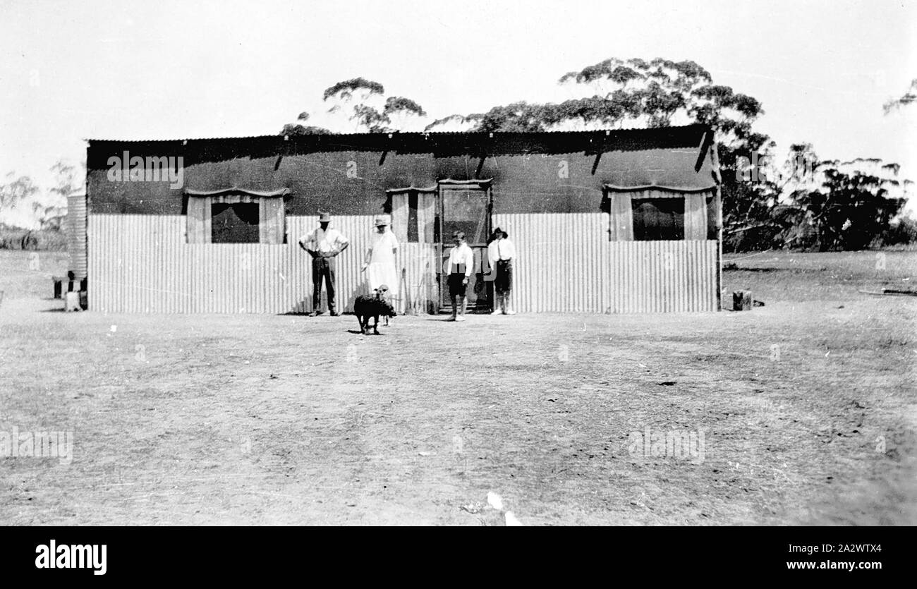 Negativo - Karawinna District, Victoria, circa 1925, membri della famiglia Allen davanti alla loro casa che è costruito di ferro ondulato e hessian e viene sostenuta da montanti. Una veranda si estende attraverso la parte anteriore Foto Stock