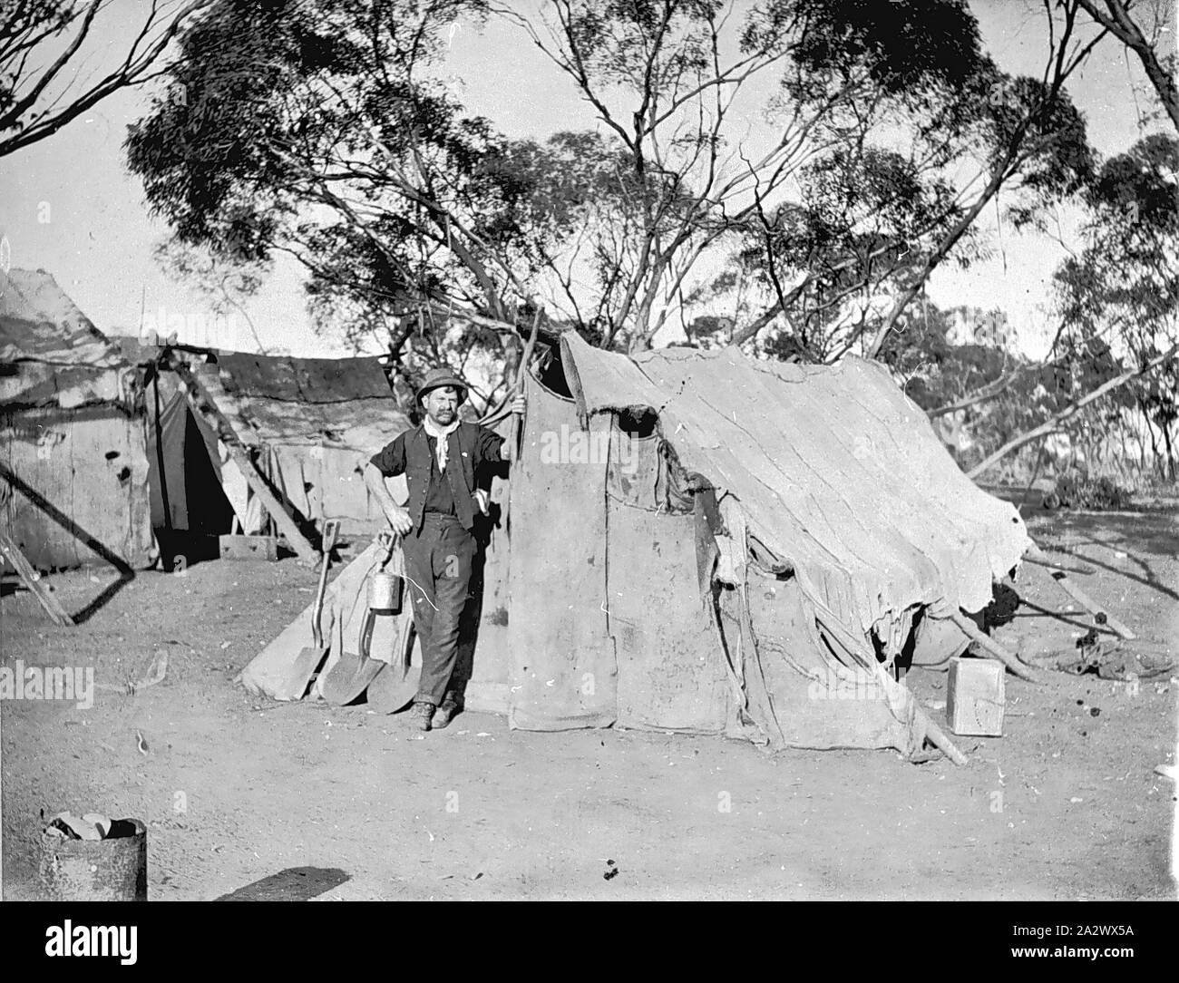 Negativo - Goulburn Valley, Victoria, circa 1915, un uomo di fronte ad una tenda costruito di Hessian. Ci sono simili capanne dietro di lui. Una vanga, due pale e un billy può sono sostennero contro la tenda Foto Stock