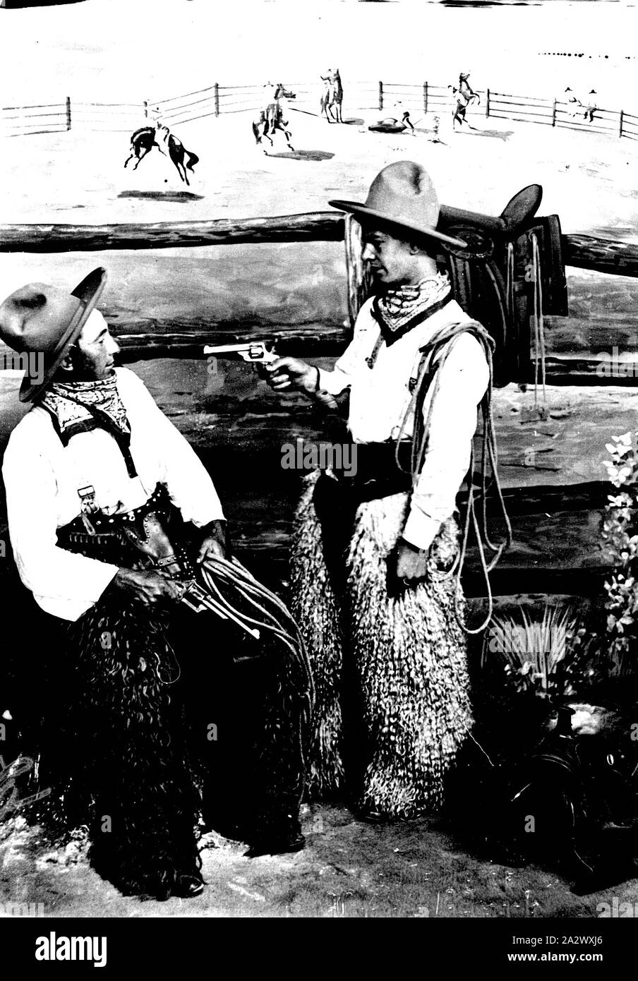 Negativo - St Kilda, Victoria, circa 1919, pone una fotografia di due uomini vestiti come i cowboys, un uomo indicando una pistola all'altra. Essi sono al Luna Park e sono in piedi di fronte a uno sfondo raffigurante una scena di rodeo Foto Stock