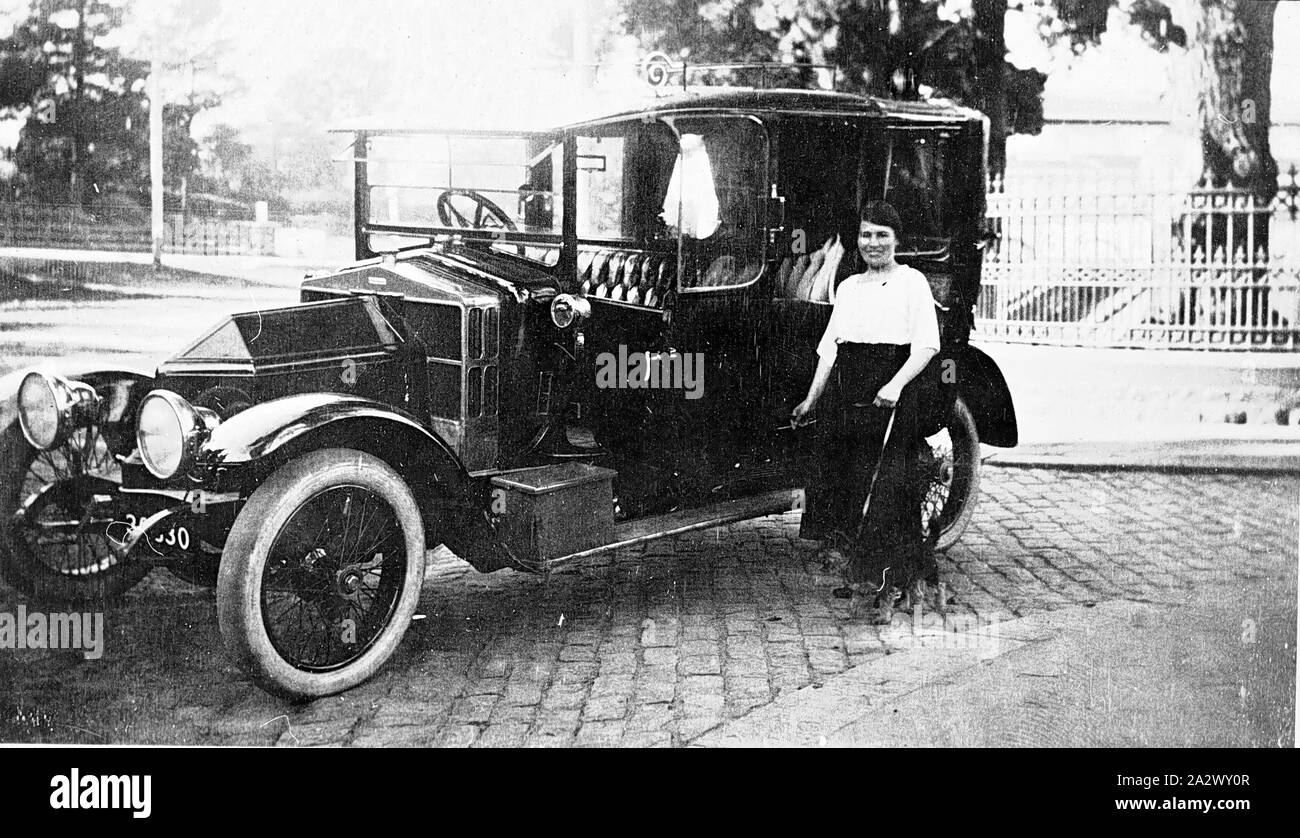 Negativo - Geelong, Victoria, circa 1920, una donna e cane in piedi accanto a un'auto. La macchina è su una pietra blu strada asfaltata e vi è un ferro battuto recinzione dietro di lei Foto Stock