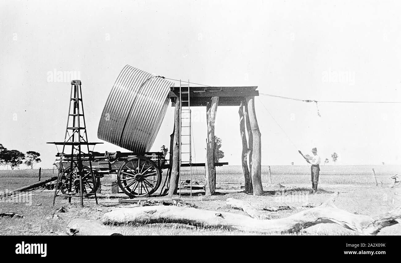 Negativo - Nhill District, Victoria, 1920, sollevando un serbatoio di acqua su un piedistallo sul Heatherlea farm. I cavi sono collegati al serbatoio che è ancora parzialmente in appoggio su un carro Foto Stock