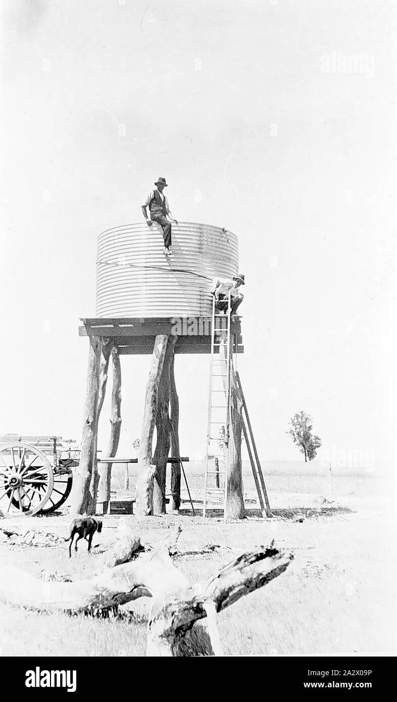 Negativo - Nhill District, Victoria, 1920, sollevando un serbatoio di acqua su un piedistallo sul Heatherlea farm. Il serbatoio è ora in posizione e un uomo è seduto sulla sommità di esso Foto Stock