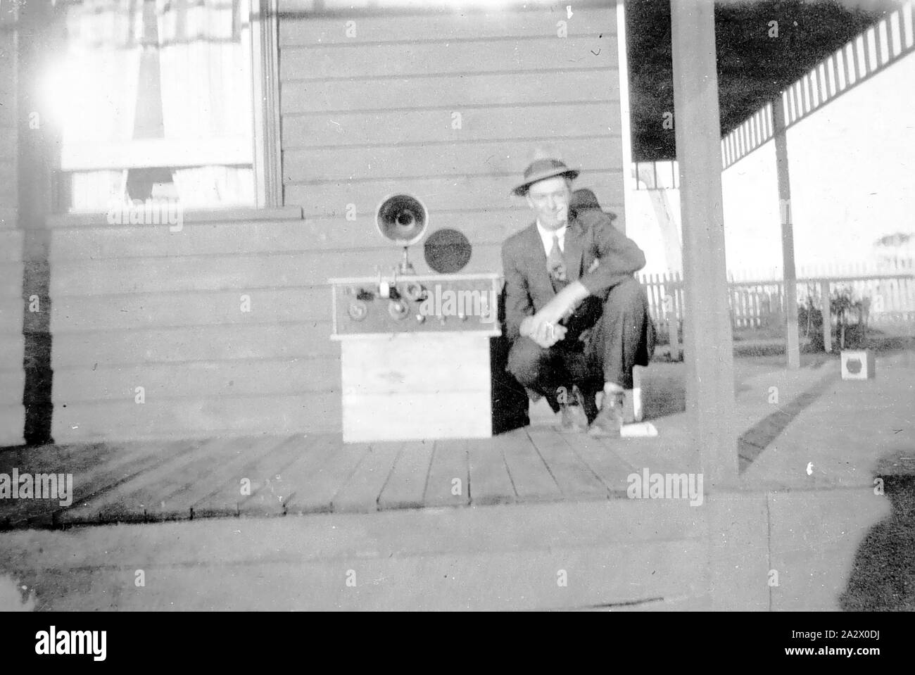 Negativo - Western District (?), Victoria, circa 1925, un uomo con un apparecchio radio. Egli è accovacciata accanto ad esso su una veranda Foto Stock