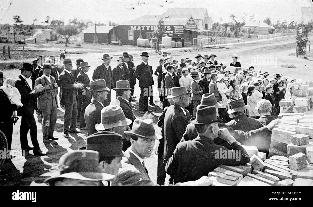 Negativo - Ouyen, Victoria, circa 1920, una folla di gente a guardare qualcosa a destra. Vi è una pila di mattoni in primo piano e il negozio di Matthews, tankmaker attraversata la strada Foto Stock