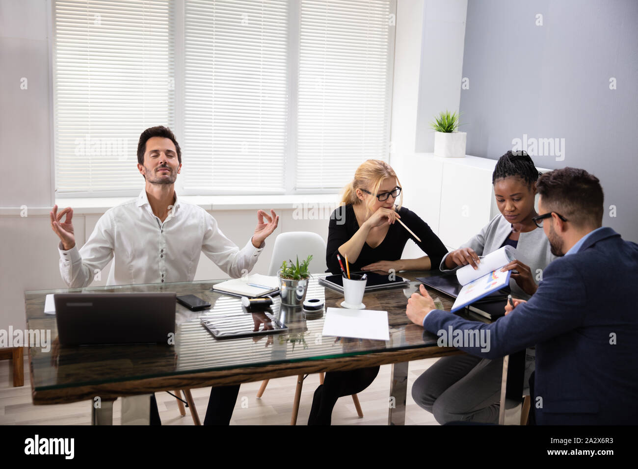 Giovane Maschio lavoratore di ufficio meditando al lavoro ignorando stressante sale riunioni con i colleghi Foto Stock