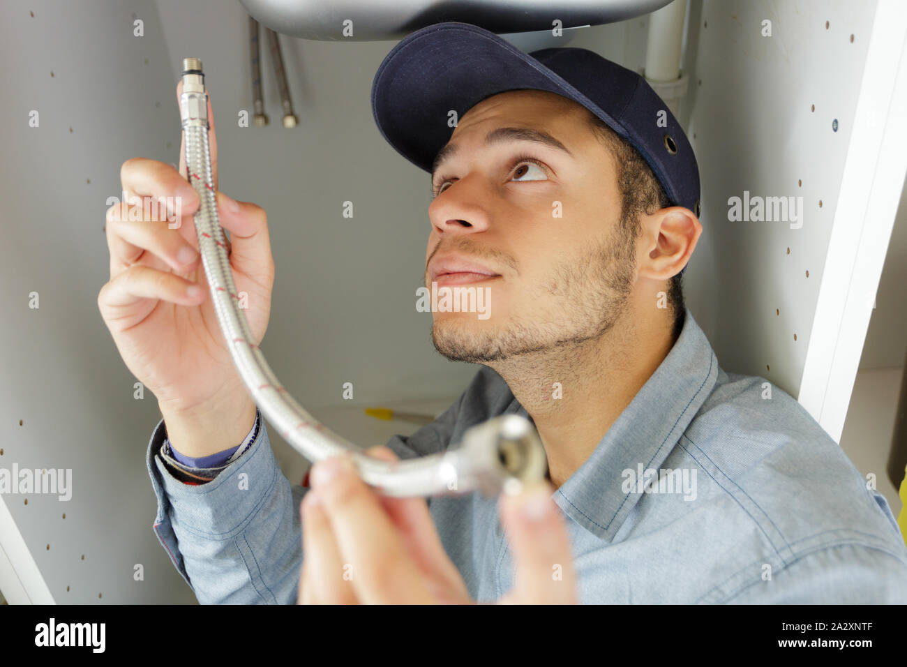 Giovane maschio plumber raccordo tubo flessibile sotto il lavello Foto Stock