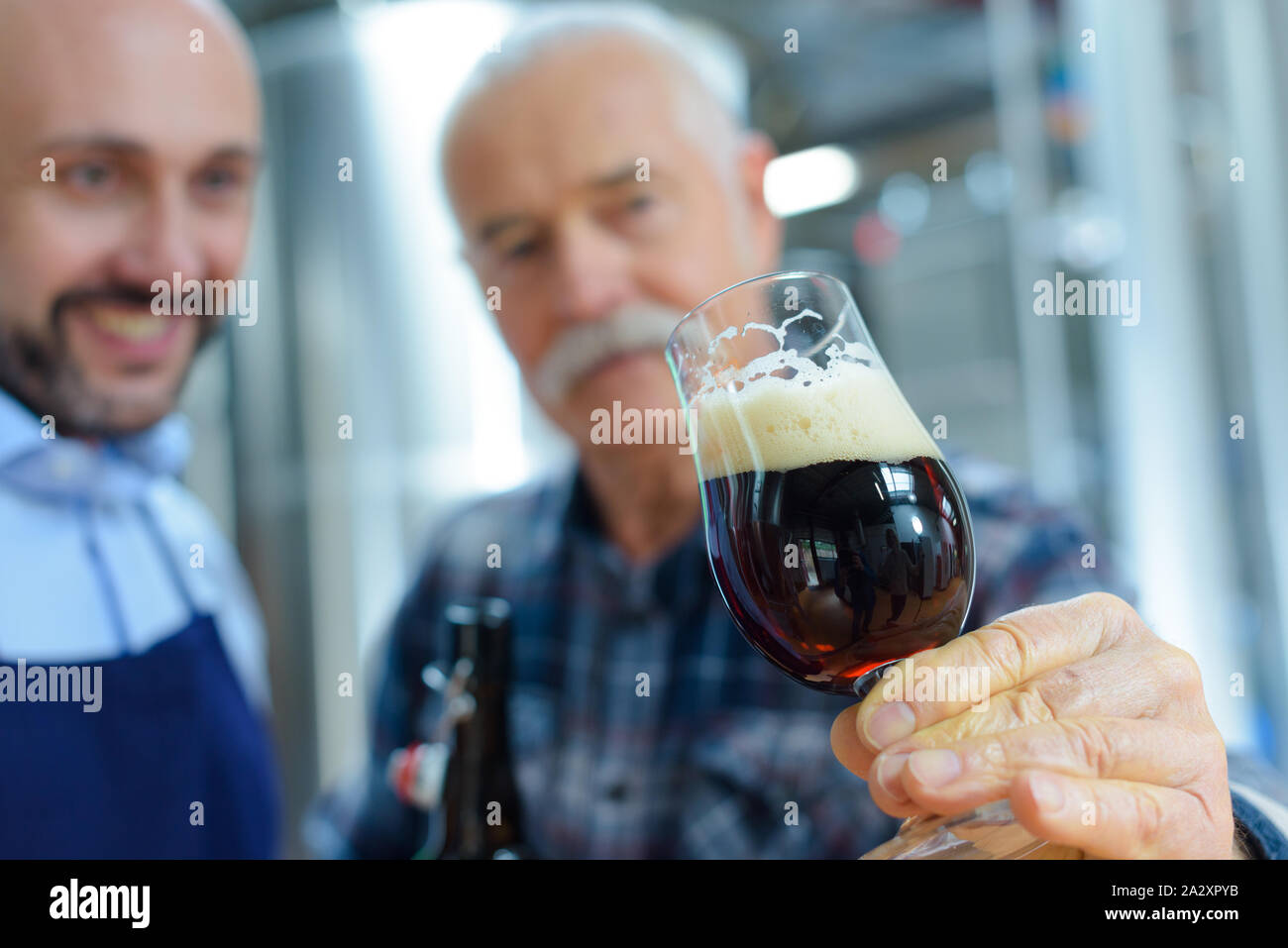 Gli uomini in birreria vetro inclinabile per esaminare ale Foto Stock