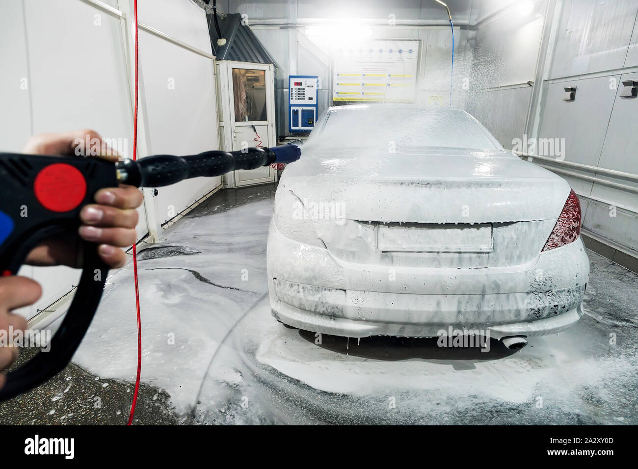 Lavaggio auto con schiuma in auto la stazione di lavaggio. Un uomo di  schiuma spray sulla vettura da un apposito spray. Lavoratore di sesso  maschile lavare la vettura con idropulitrice ad alta