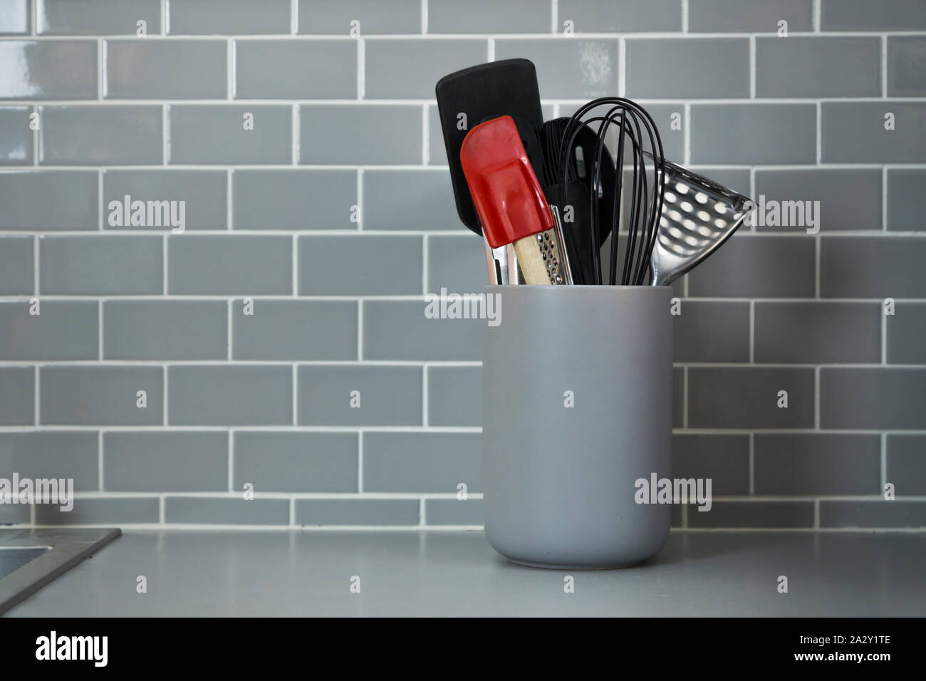 Un vaso di utensili da cucina contro le piastrelle da cucina. Foto Stock