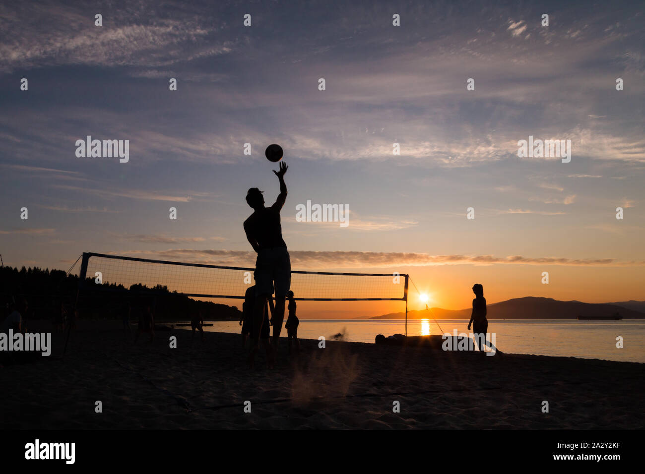 Gruppo di giovani che giocano a Beach volley e che si contornano al tramonto a Kits Beach a Vancouver, British Columbia. Foto Stock