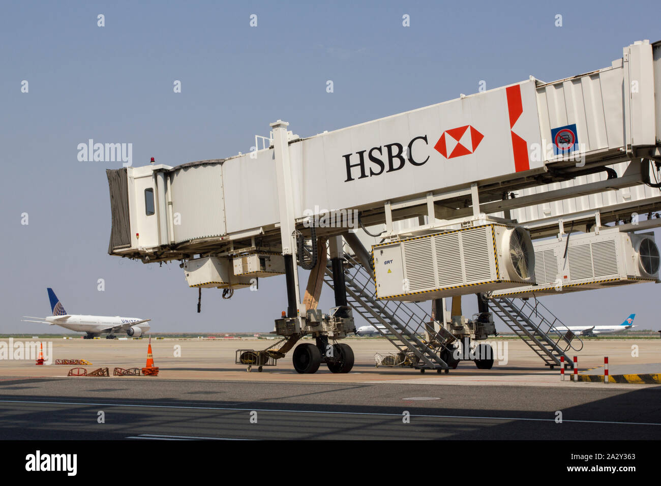 Un jet bridge con il logo HSBC presso l'affollato Aeroporto di Shanghai Pudong, con diversi aeroplani che si allineano sulla pista per la partenza sullo sfondo. Foto Stock