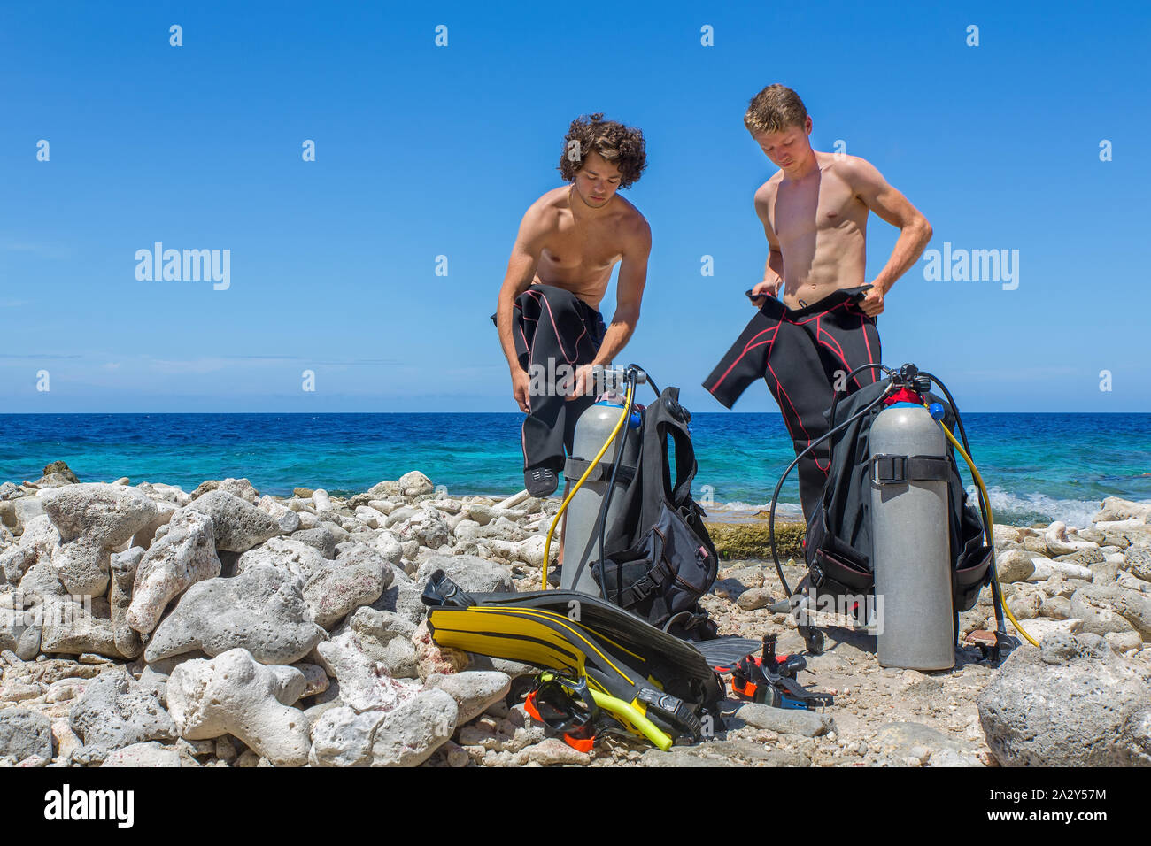 Due subacquei olandese cambiando i vestiti in spiaggia a Bonaire con mare blu Foto Stock