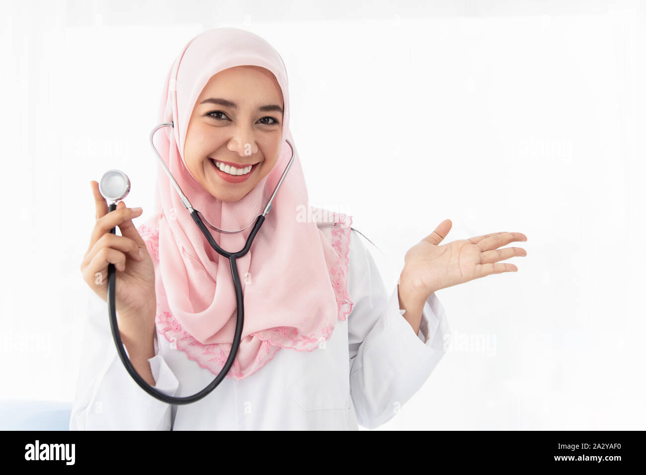 Ritratto di una giovane e bella donna musulmana medico mostra il suo lato sinistro e indossa uno stetoscopio in piedi e sorrisi in una camera di esame in OSP Foto Stock