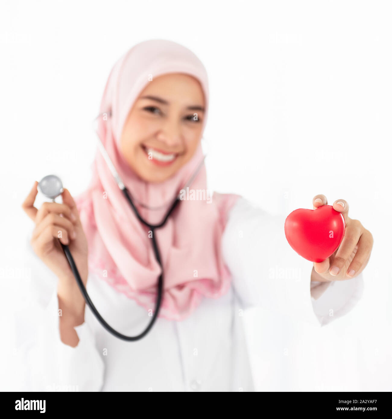 Ritratto di giovane e bella donna musulmana medico mostra un cuore rosso sul lato sinistro e indossa uno stetoscopio in piedi e sorrisi in un esame roo Foto Stock