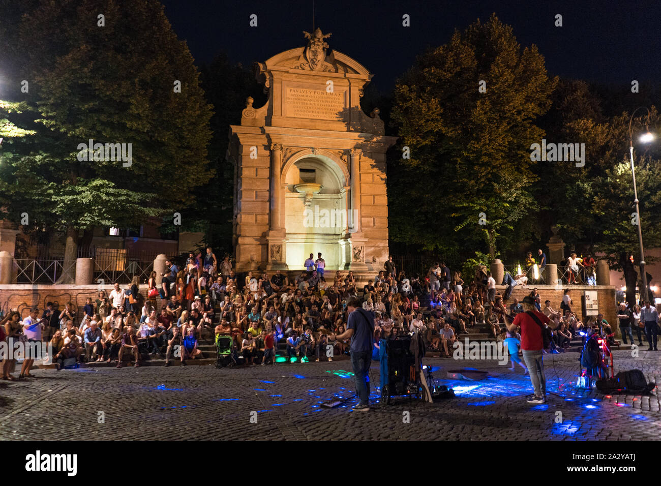 La vita notturna a Trastevere. Streetmusic di fronte alla fontana di Piazza Trilusso. Fontanone di Ponte Sisto di Roma di notte. Un sacco di gente seduta Foto Stock