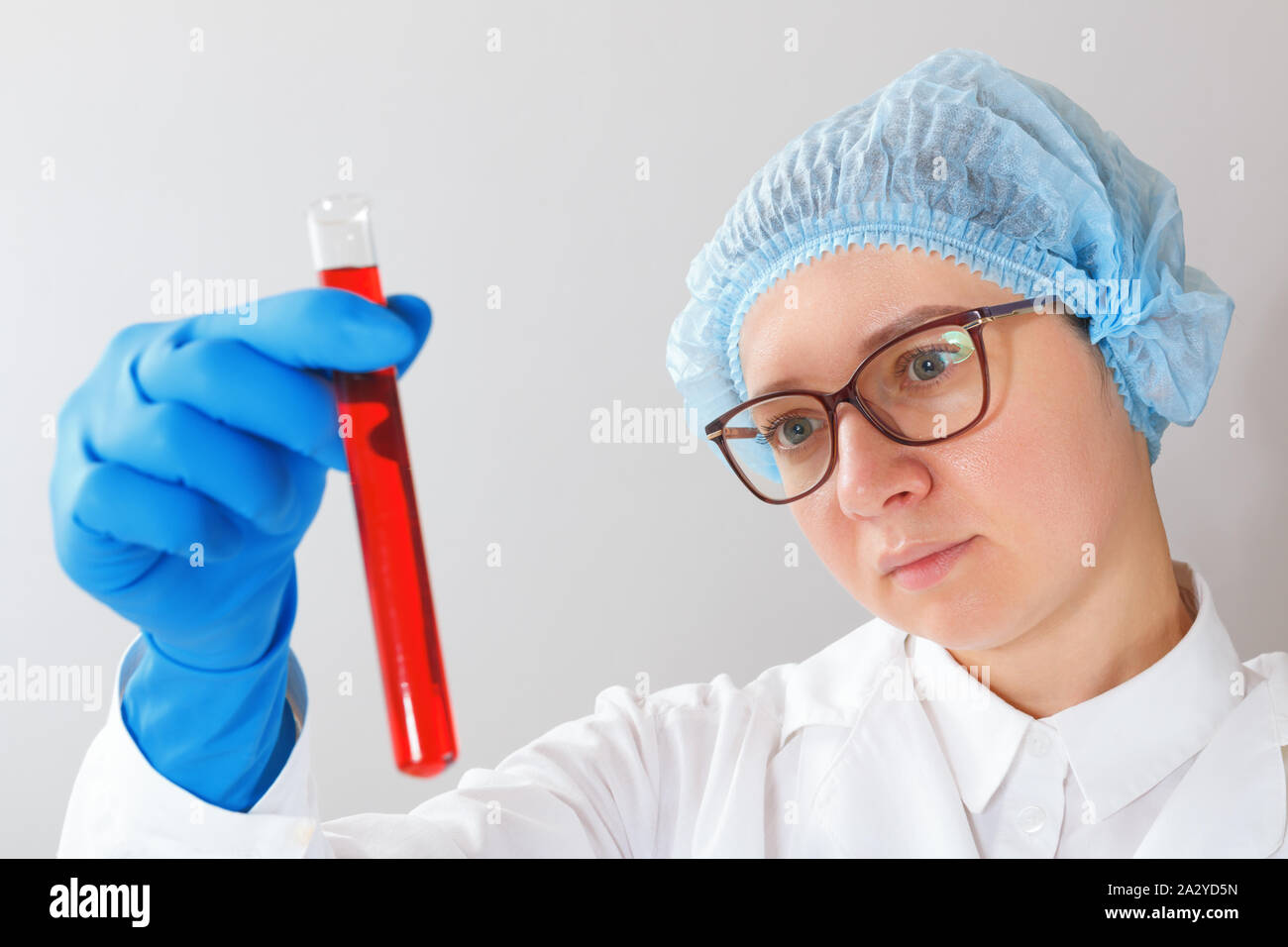 Una donna scienziato con gli occhiali sta conducendo un esperimento in un laboratorio, tenendo una provetta con liquido rosso nelle sue mani. Foto Stock