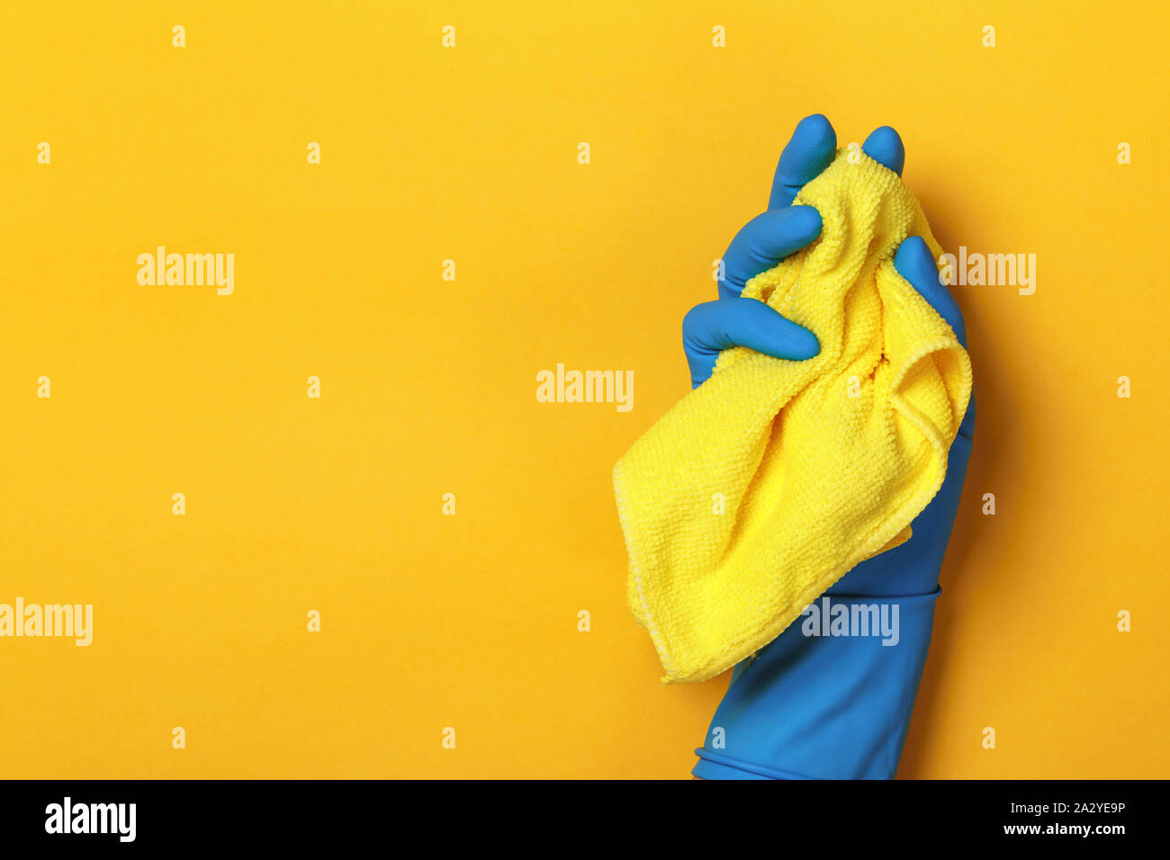 Una mano in una protezione di blue guanto contiene un panno giallo su sfondo giallo sfondo colorato. Foto Stock