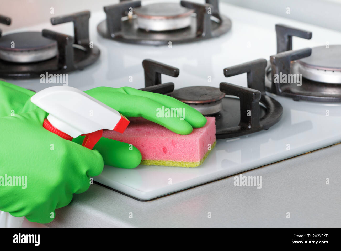 Primo piano della mano nel guanto protettivo tenendo la bottiglia spray e spugna. La pulizia della cucina, fornello a gas. Foto Stock