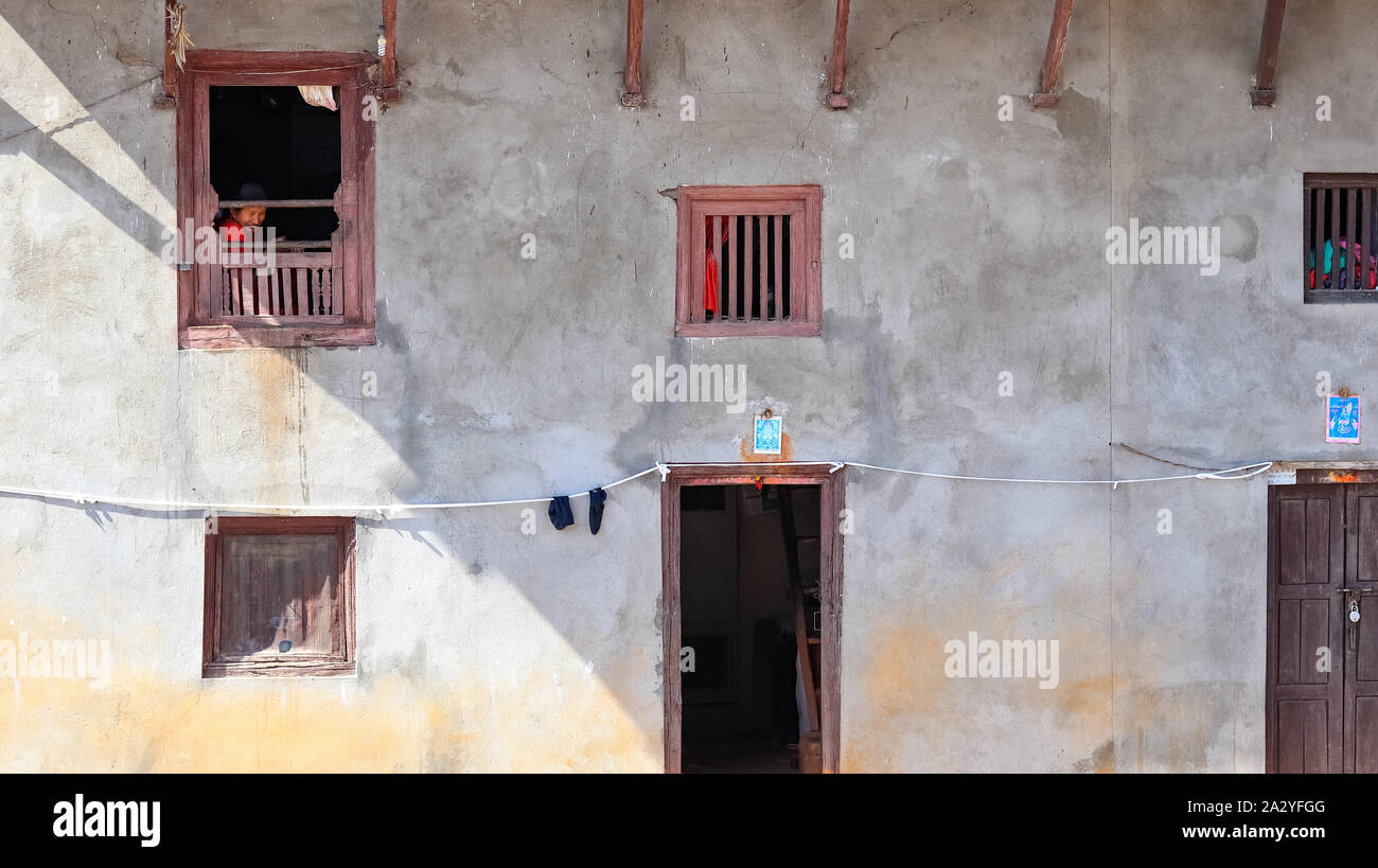Vecchia donna guardando fuori di una tradizionale casa nepalese Foto Stock