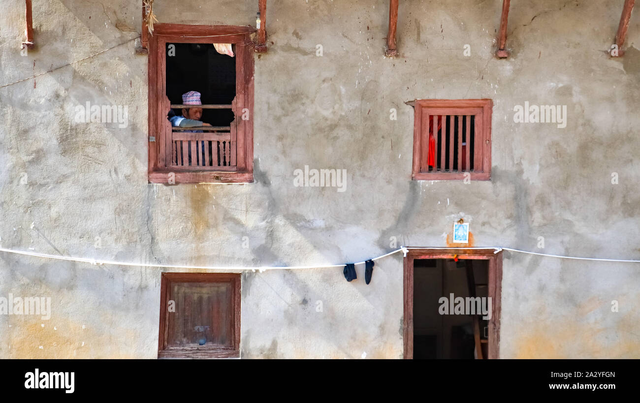 Il vecchio uomo che guarda fuori di una tradizionale casa nepalese Foto Stock