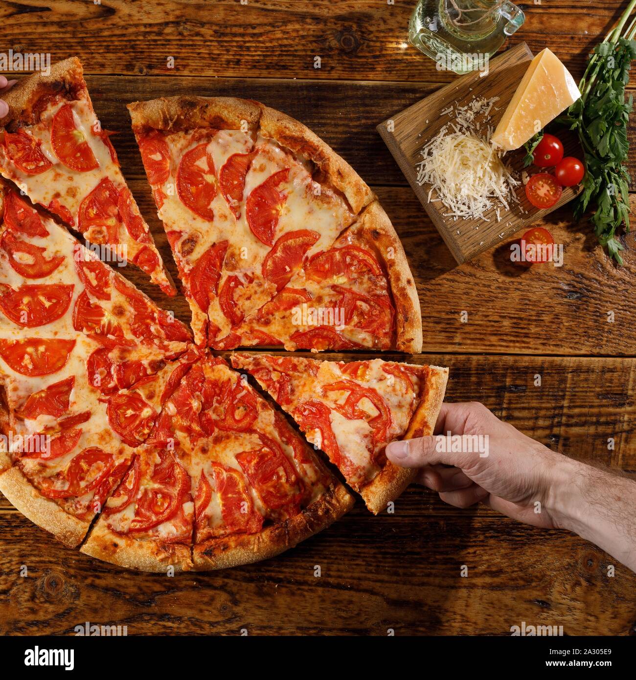 Pizza Margherita su un tavolo di legno. Ancora vita con mano e ingredienti. Vista dall'alto. Square. Foto Stock