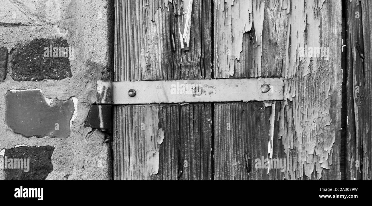 Dettaglio della finestra di casa rurale con incrinato la vernice e la ruggine cerniere, sul muro di mattoni e pietre antiche. Foto Stock